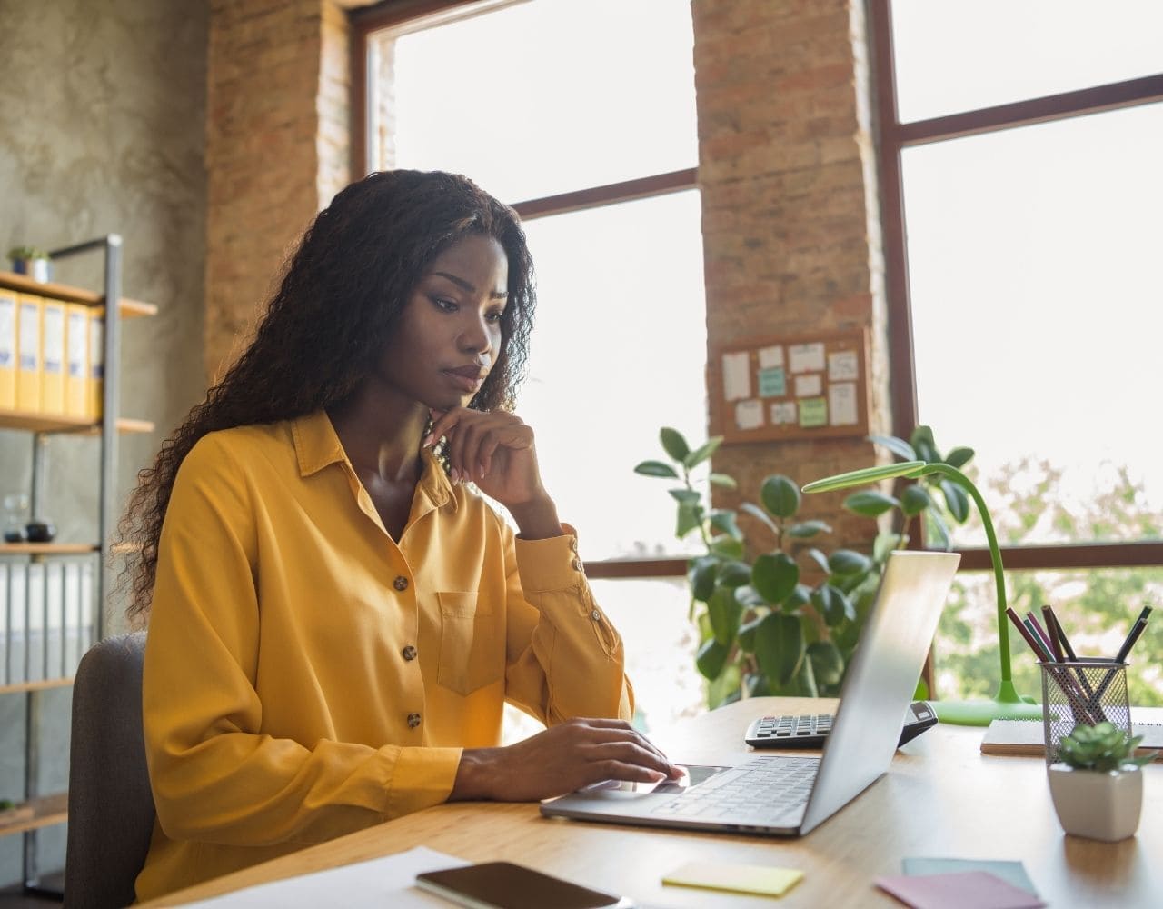 Femme entrepreneur concentrée travaillant sur son ordinateur portable dans un bureau lumineux pour remplir sa déclaration de revenus professionnels et sociale unifiée.